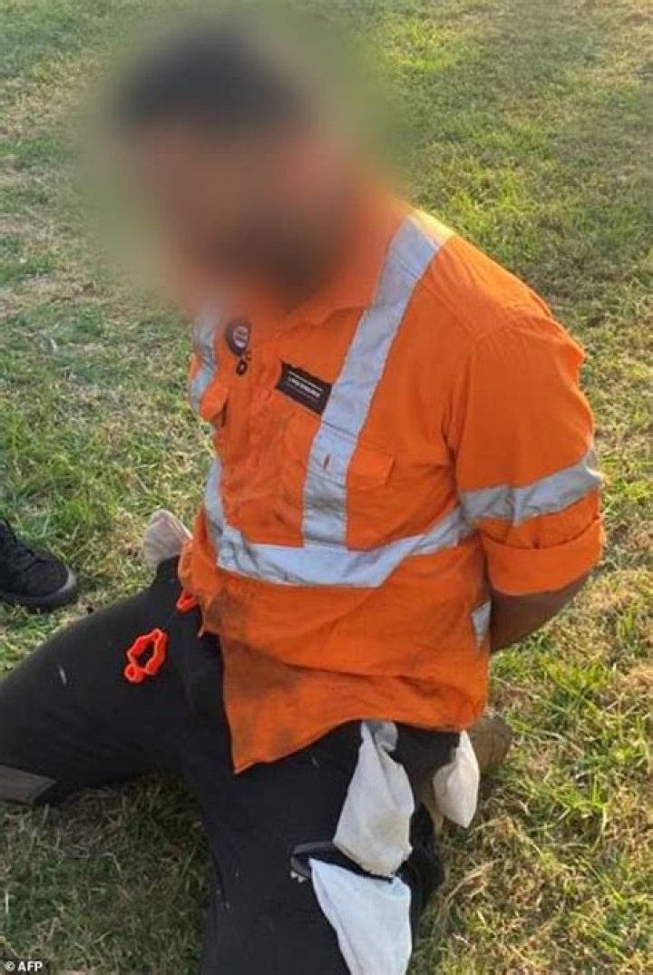 A tradie is seen kneeling with his hands tied behind his back after being arrested following raids