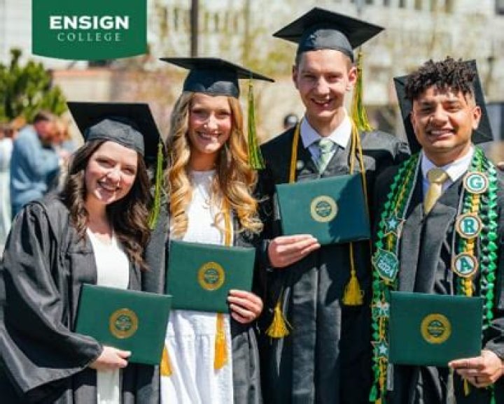 Ensign College graduates, including one holding a flag, line up for processional outside the Assembly Hall.