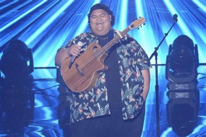 Iam Tongi holds a microphone and stands on a stage while performing on &ldquo;American Idol.&rdquo;
