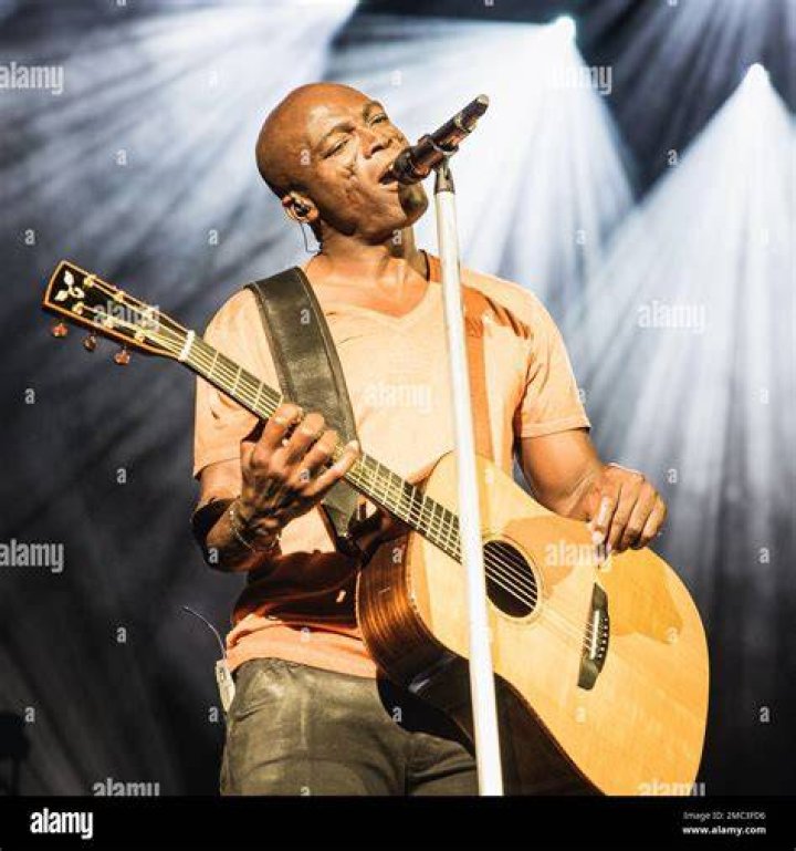 Seal performing on a stage with a guitar and singing into a microphone